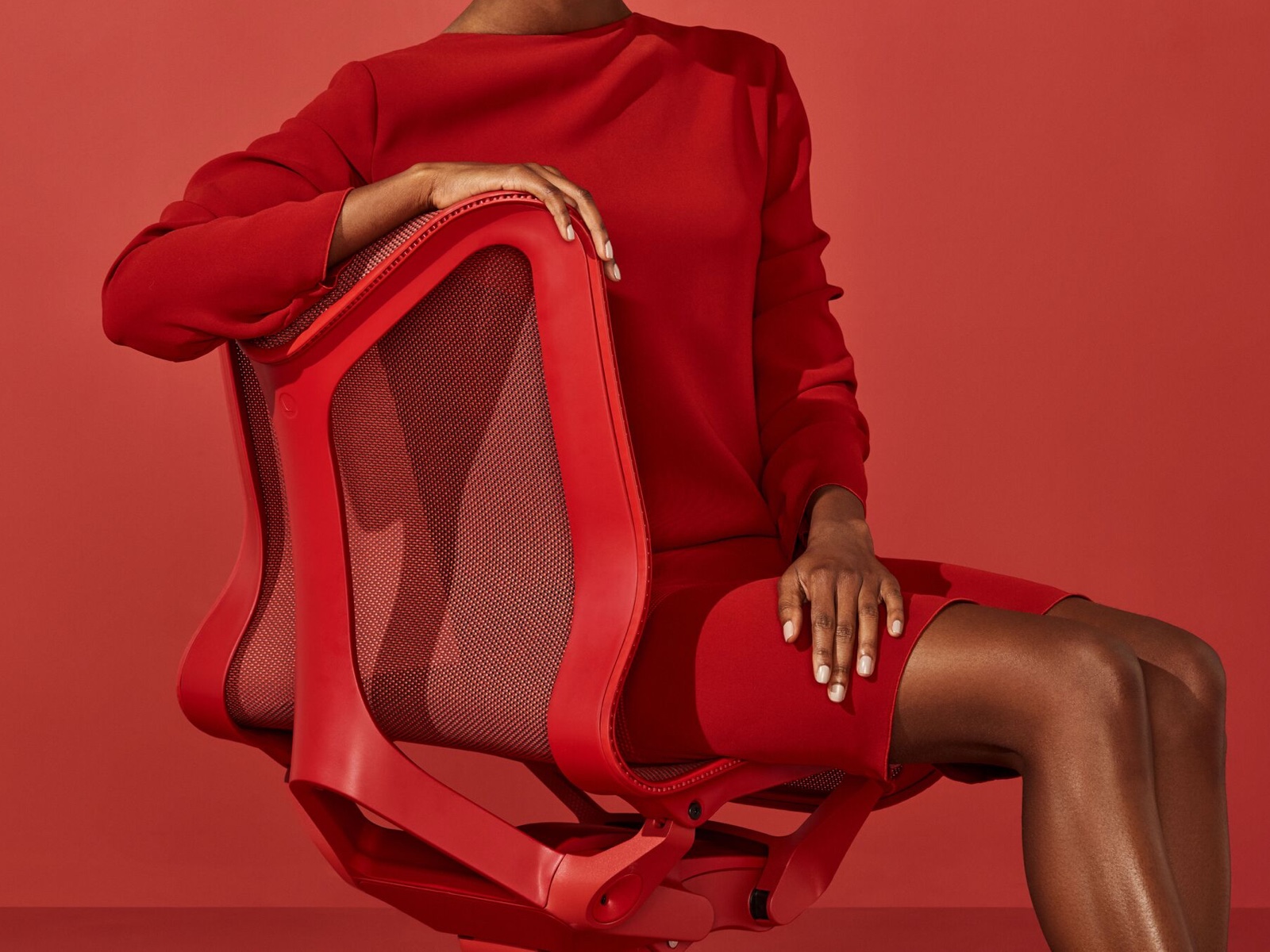 Eine Frau im roten Kleid sitzt in Canyon-Rot auf einem Cosm-Stuhl.